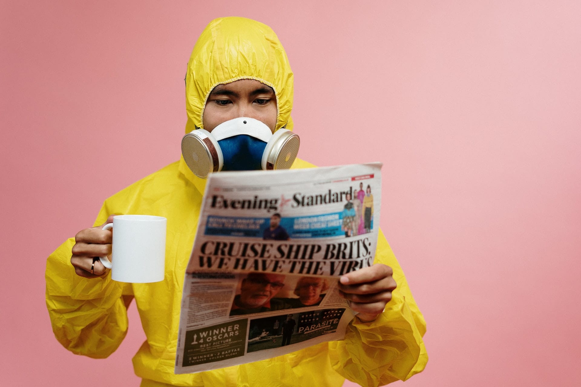 a man with PPE reading a newspaper while having a coffee